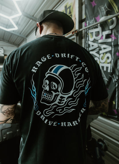 A man viewed from behind wearing a black t-shirt with a large graphic on the back. The graphic features a white and blue skull wearing a racing helmet, surrounded by the text 'RAGE DRIFT CO' and 'DRIVE HARSH'.