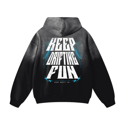 A black and gray gradient hoodie shown from the back, featuring a large graphic print with the words 'KEEP DRIFTING FUN' in white and blue lightning accents. The brand 'DRIFT DRIFT CO.